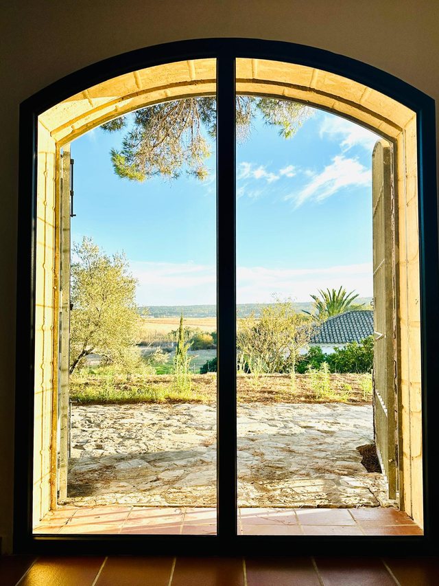 Blick von innen durch ein neu eingebautes Bogenfenster auf Olivenbäume und die andalusische Ebene