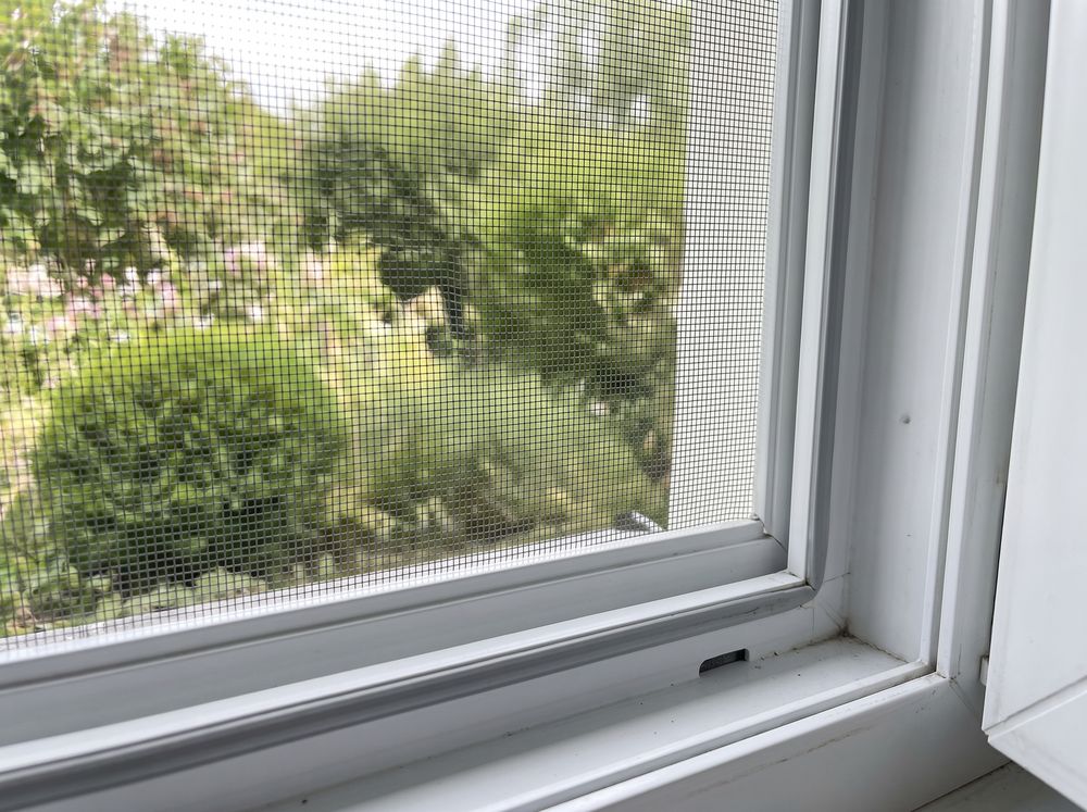 Insektenschutz-Spannrahmen in einem geöffneten Kunststofffenster, dahinter ein sommerlicher Garten