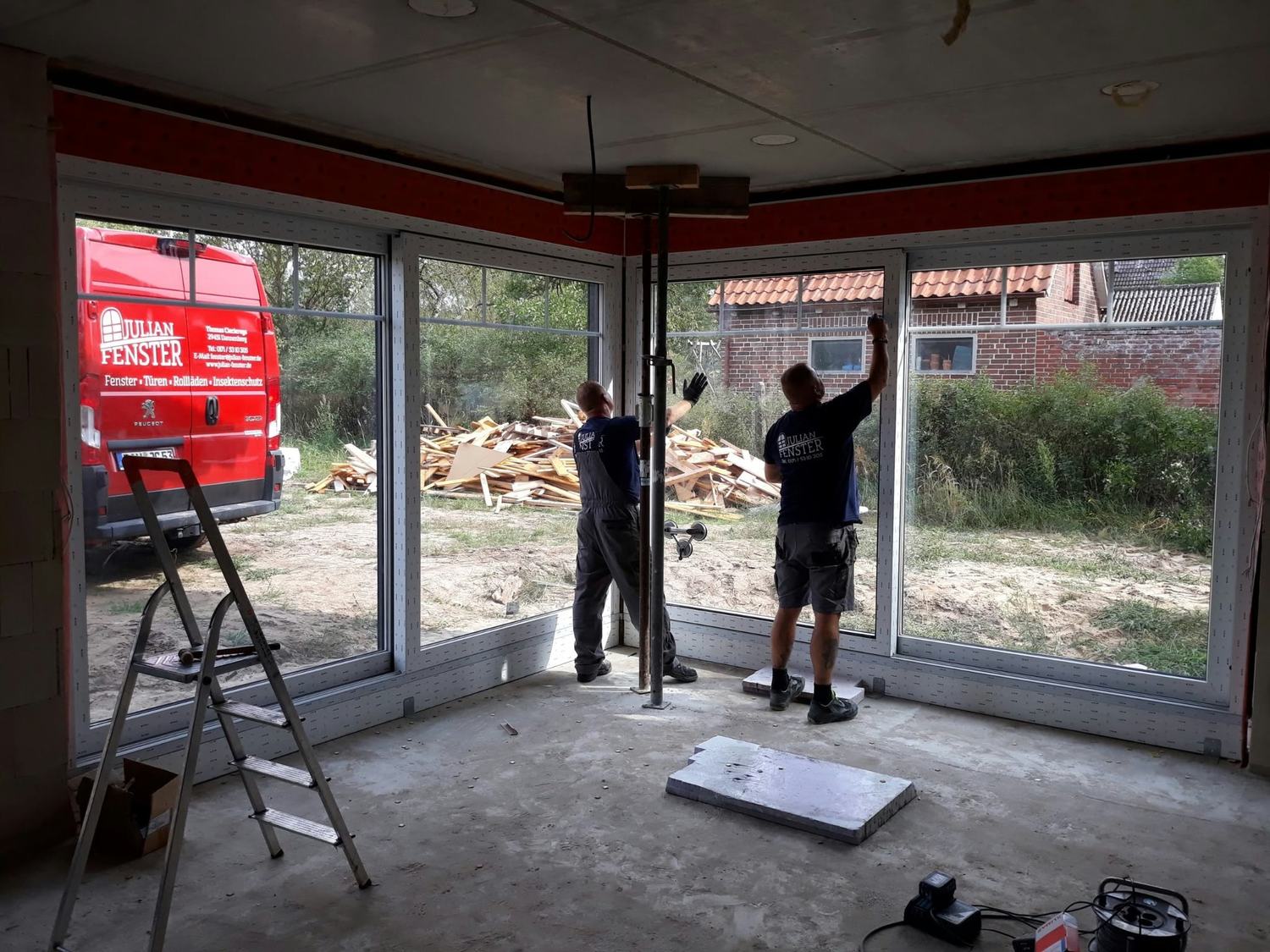 Zwei Monteure setzen eine über Eck laufende Fensterfront in einen Rohbau ein