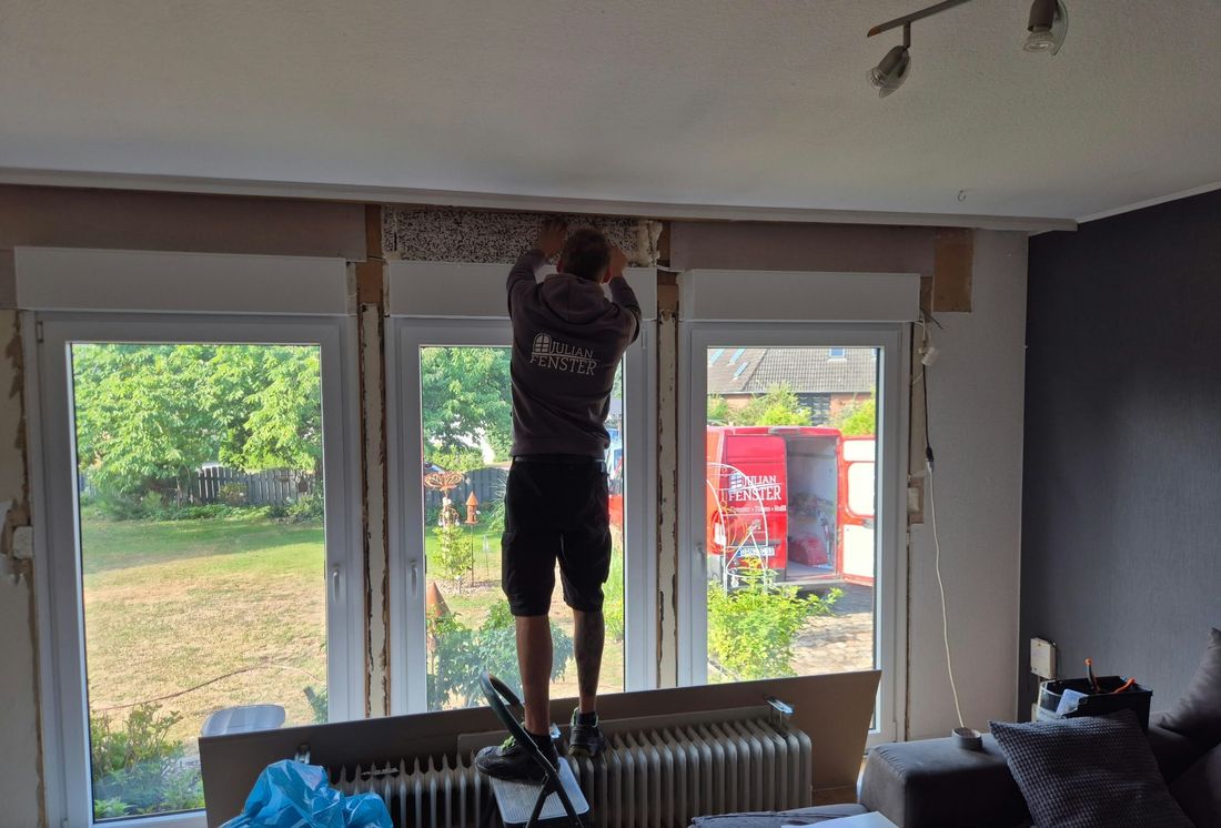 Monteur setzt eine dreiteilige Fensterfront in einem bewohnten Wohnzimmer ein