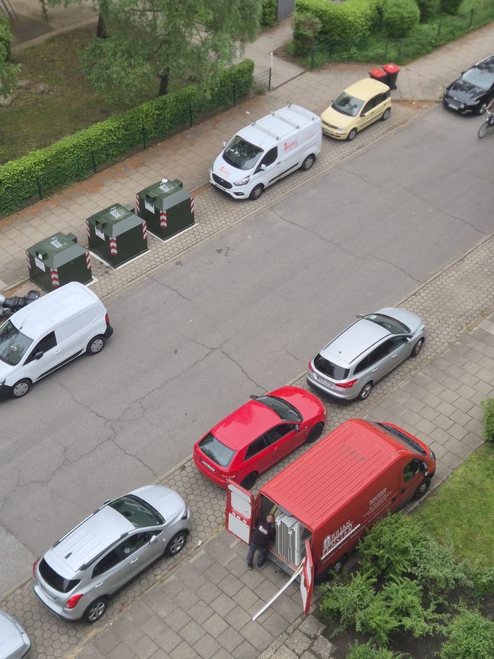 Blick von oben auf eine Wohnstraße in Hamburg, ein Monteur lädt Fensterelemente aus dem roten Firmenwagen